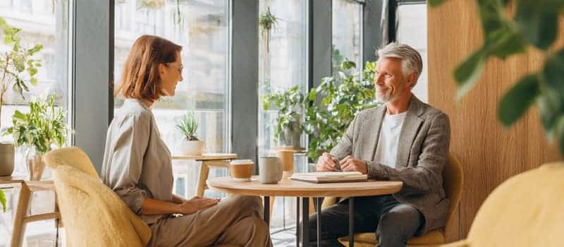 Manager et salarié en discussion calme autour d'une petite table, un carnet et deux tasses entre eux