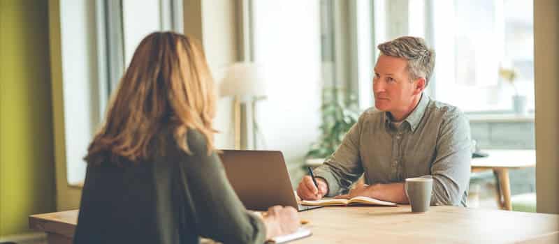 Un conseiller prend des notes pendant un entretien avec une salariée qui prépare son projet de reconversion