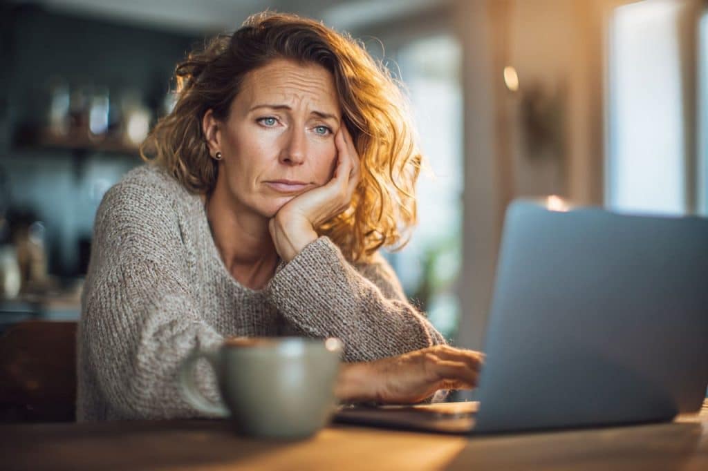 Femme hésitant devant son ordinateur, la peur de réussir au moment d'envoyer un dossier