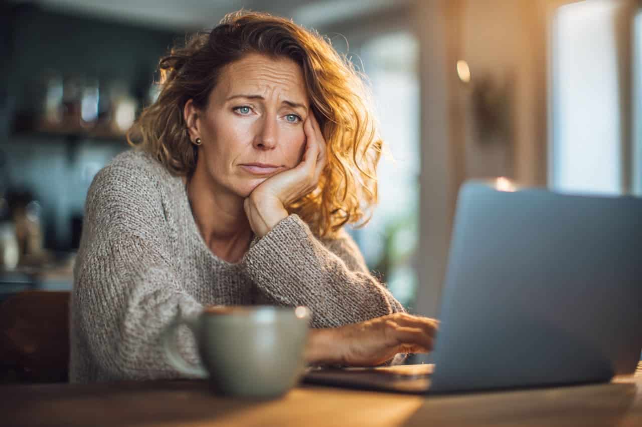 Femme hésitant devant son ordinateur, la peur de réussir au moment d'envoyer un dossier